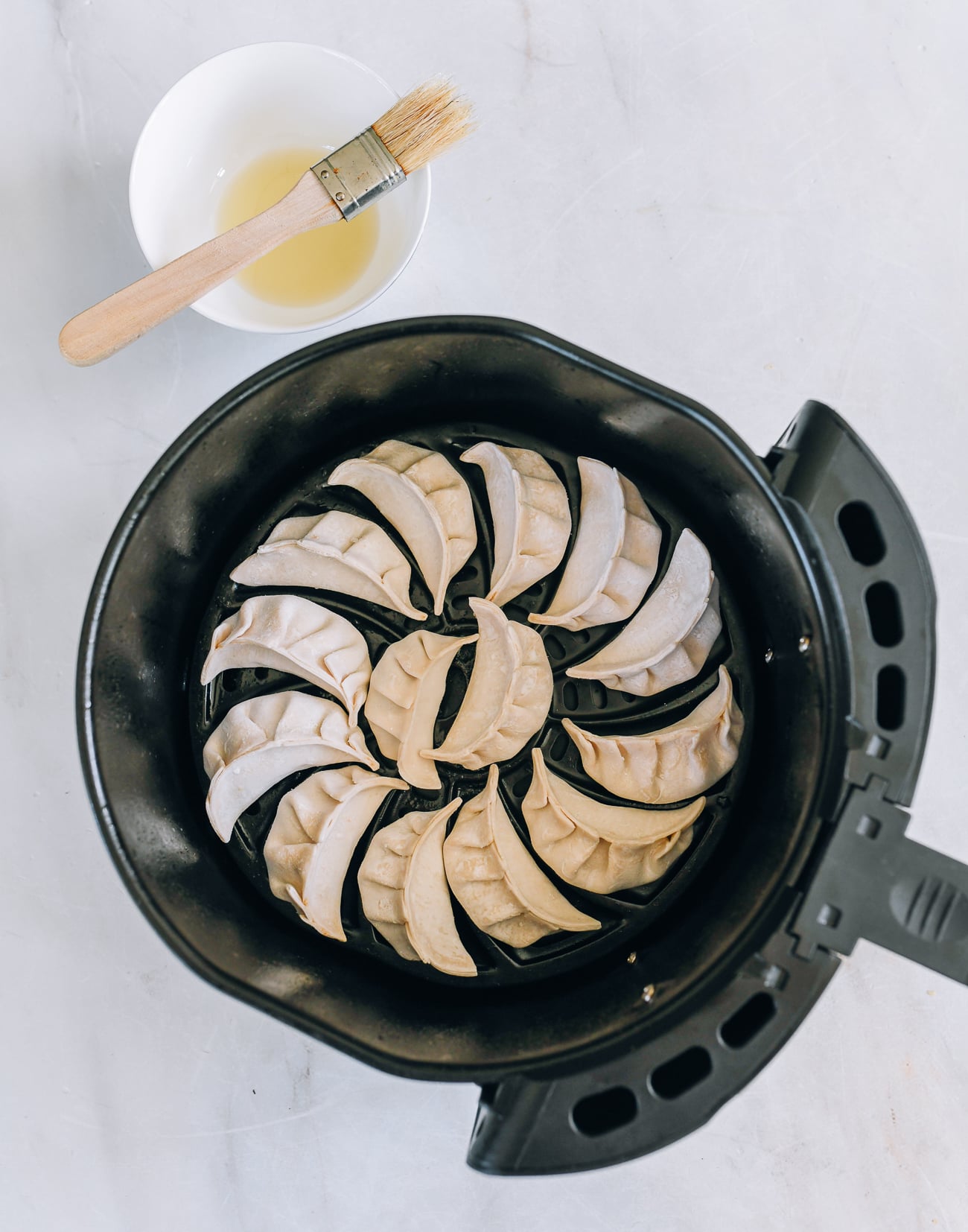 dumplings in air fryer basket with bowl of oil and pastry brush