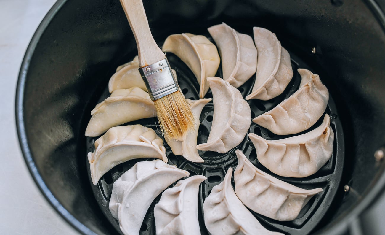 brushing dumplings in air fryer basket with oil
