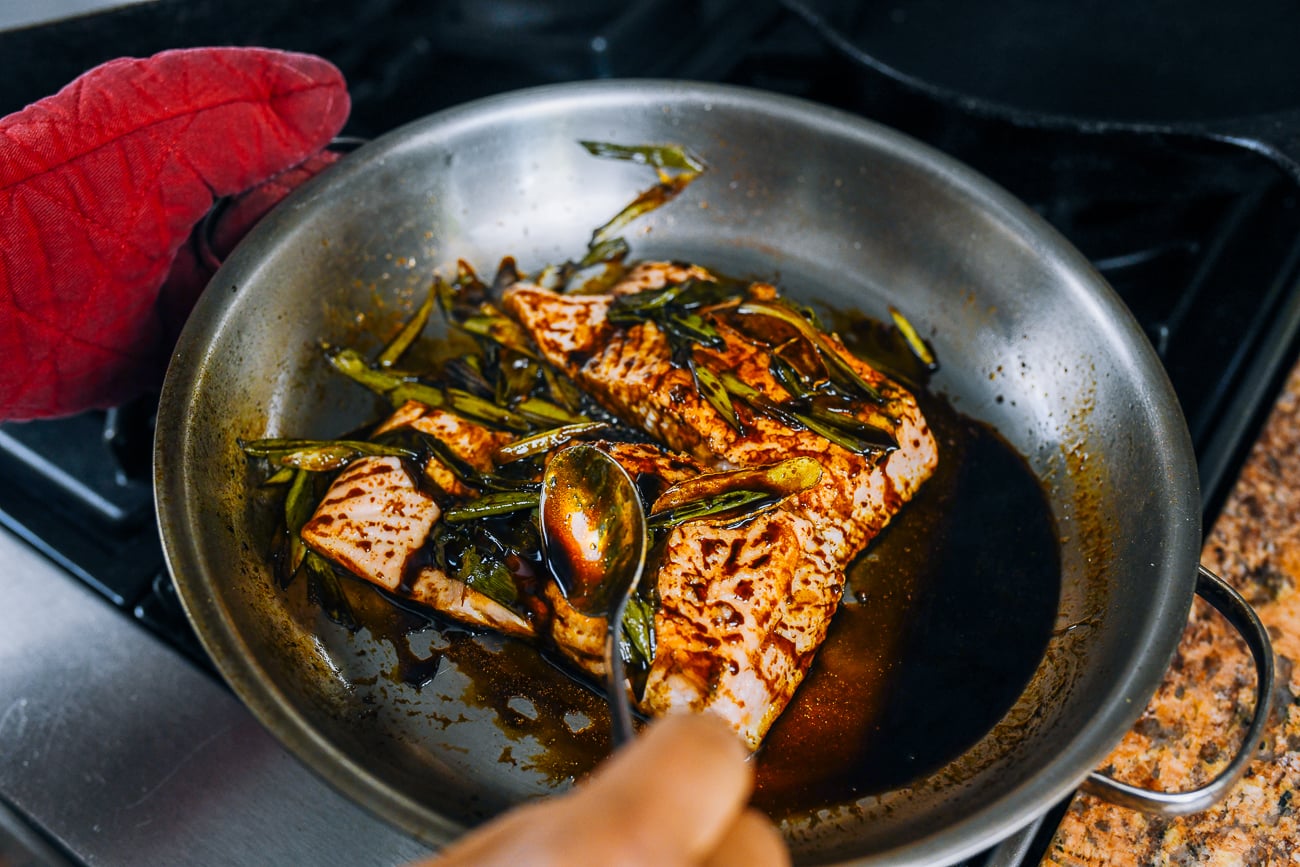 spooning sauce over salmon fillets as they cook