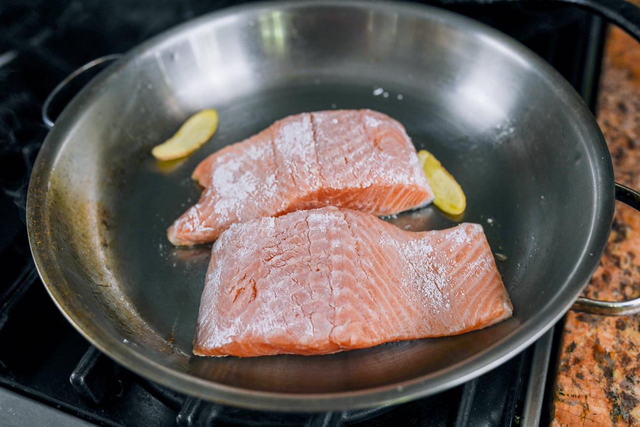 cornstarch dusted salmon fillets and ginger slices in pan