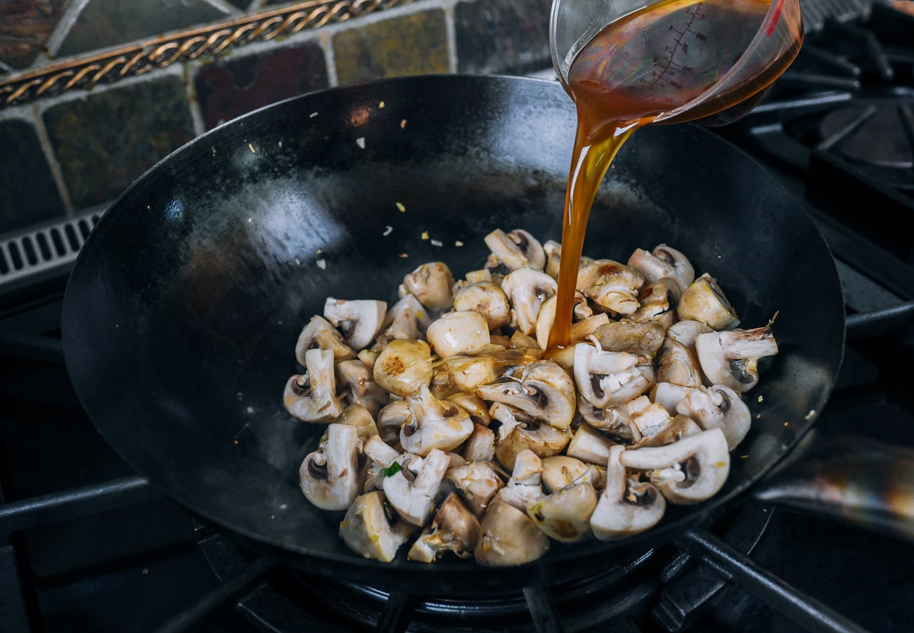 Adding chicken stock and seasoning to mushrooms