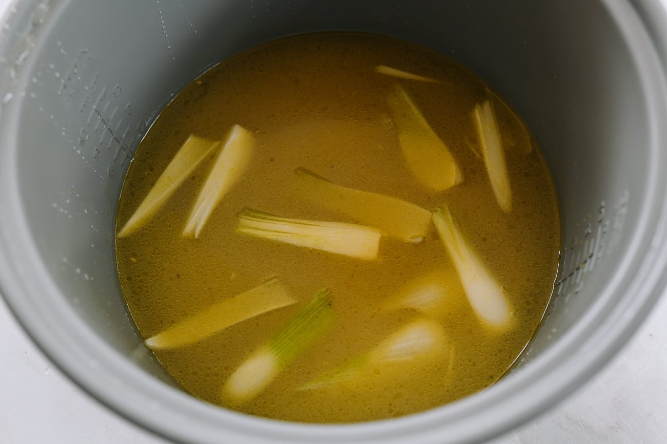 rice and stock in rice cooker with scallion and ginger