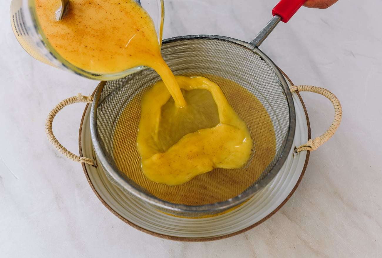pouring egg mixture through fine meshed strainer into heatproof dish