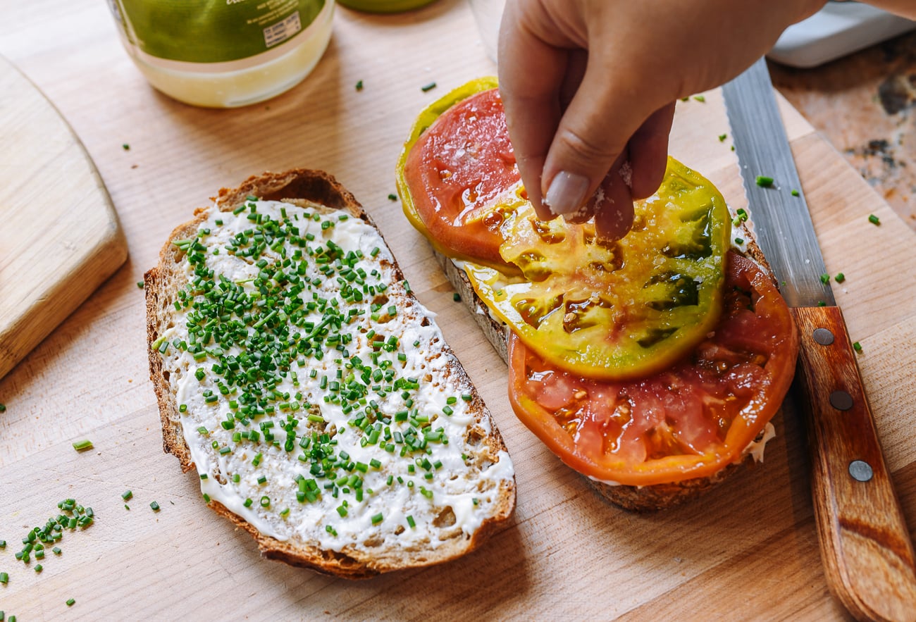 sprinkling salt on tomato sandwich