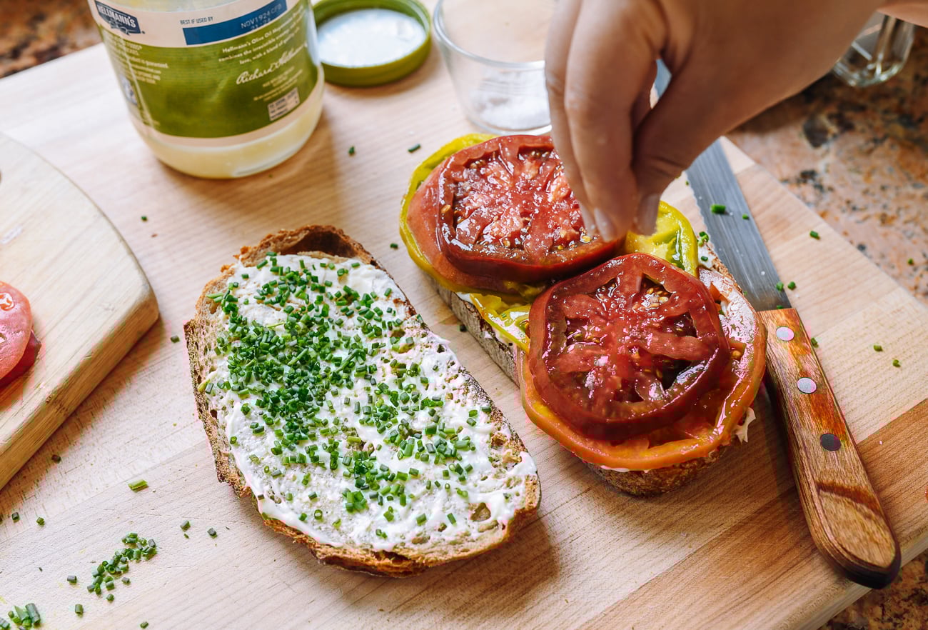sprinkling salt on tomato sandwich