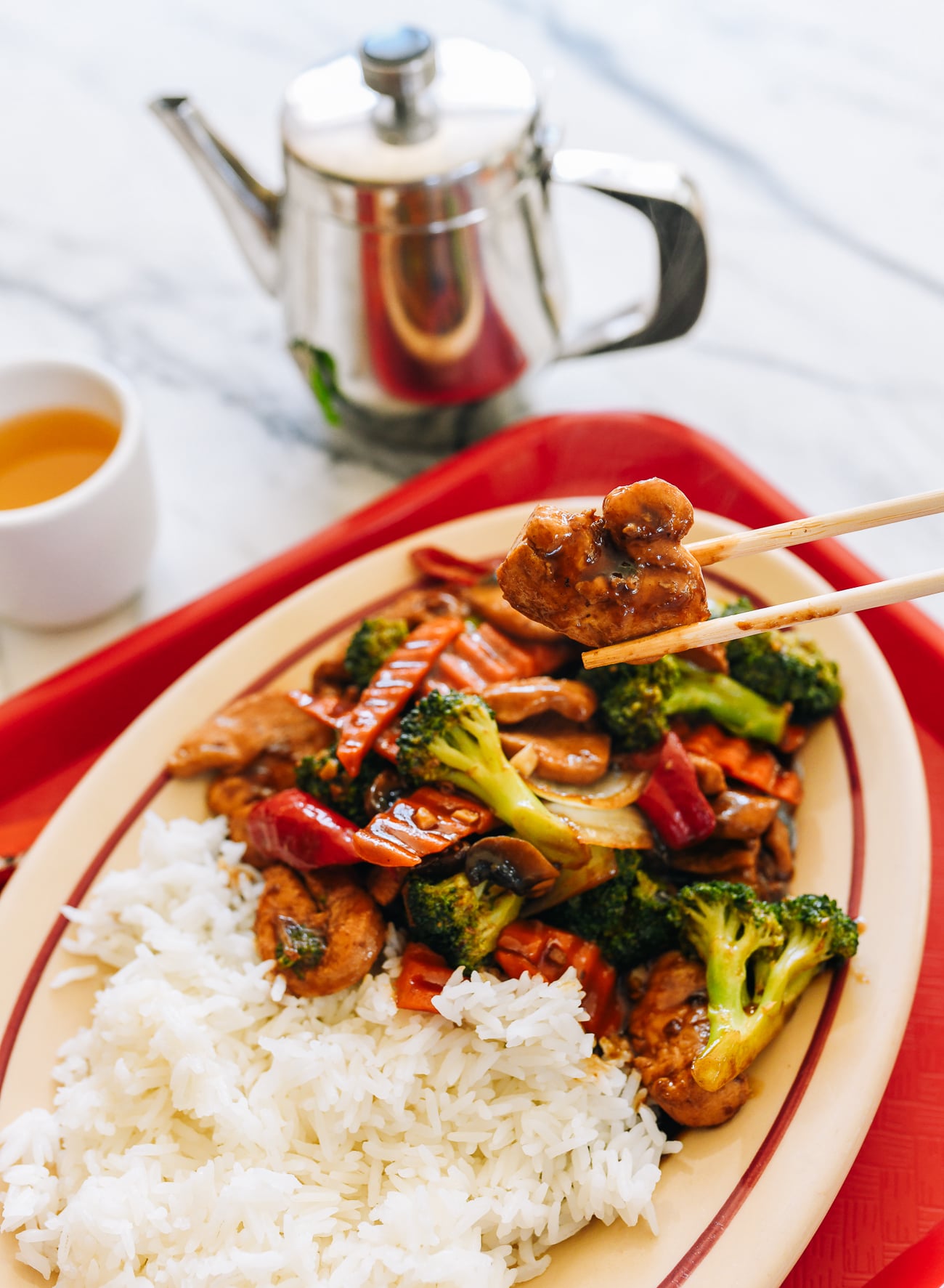 Picking up piece of Chinese takeout chicken with mixed vegetables with chopsticks