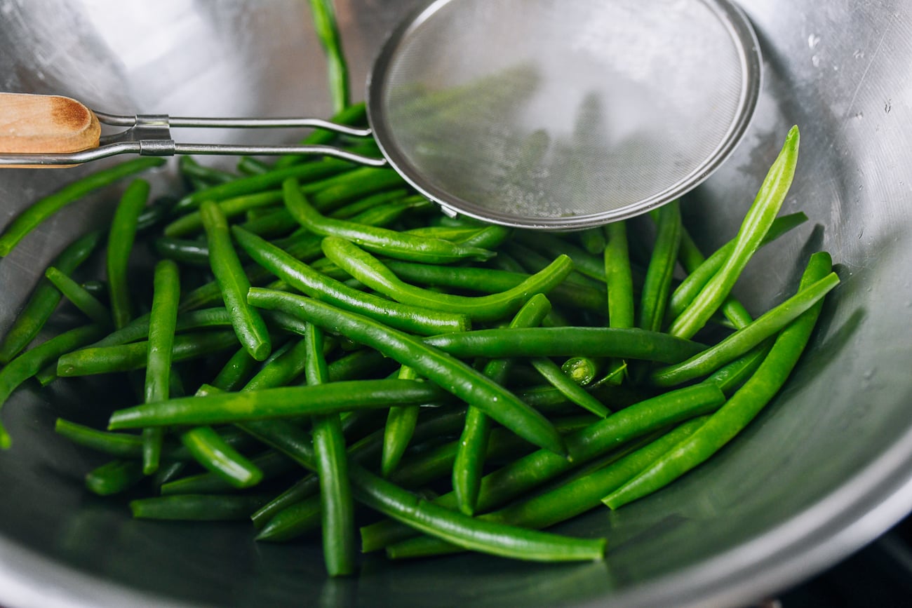 removing blanched green beans from boiling water with strainer