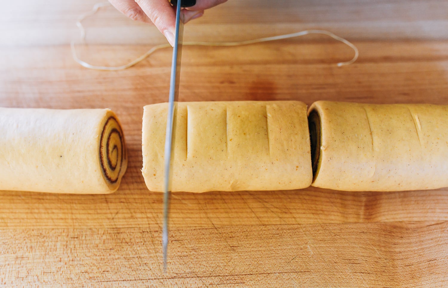 scoring log of dough to cut cinnamon rolls