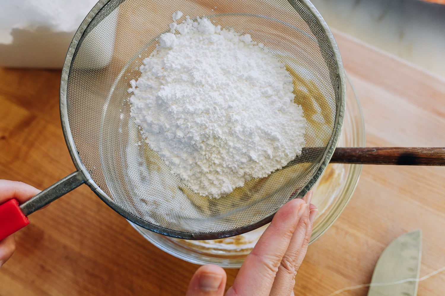 sifting powdered sugar into bowl of cream cheese and butter