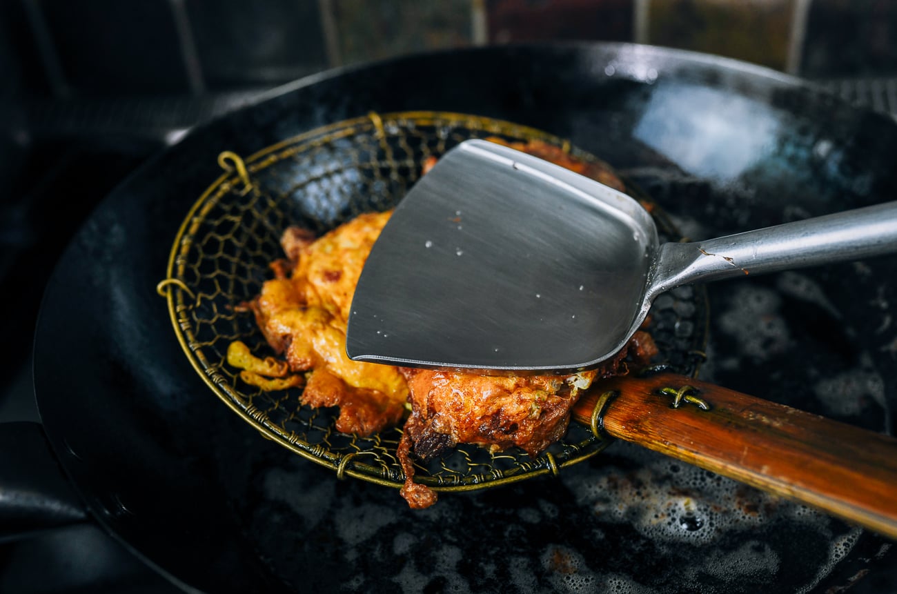 using wok spatula to squeeze excess oil out of egg foo young patty