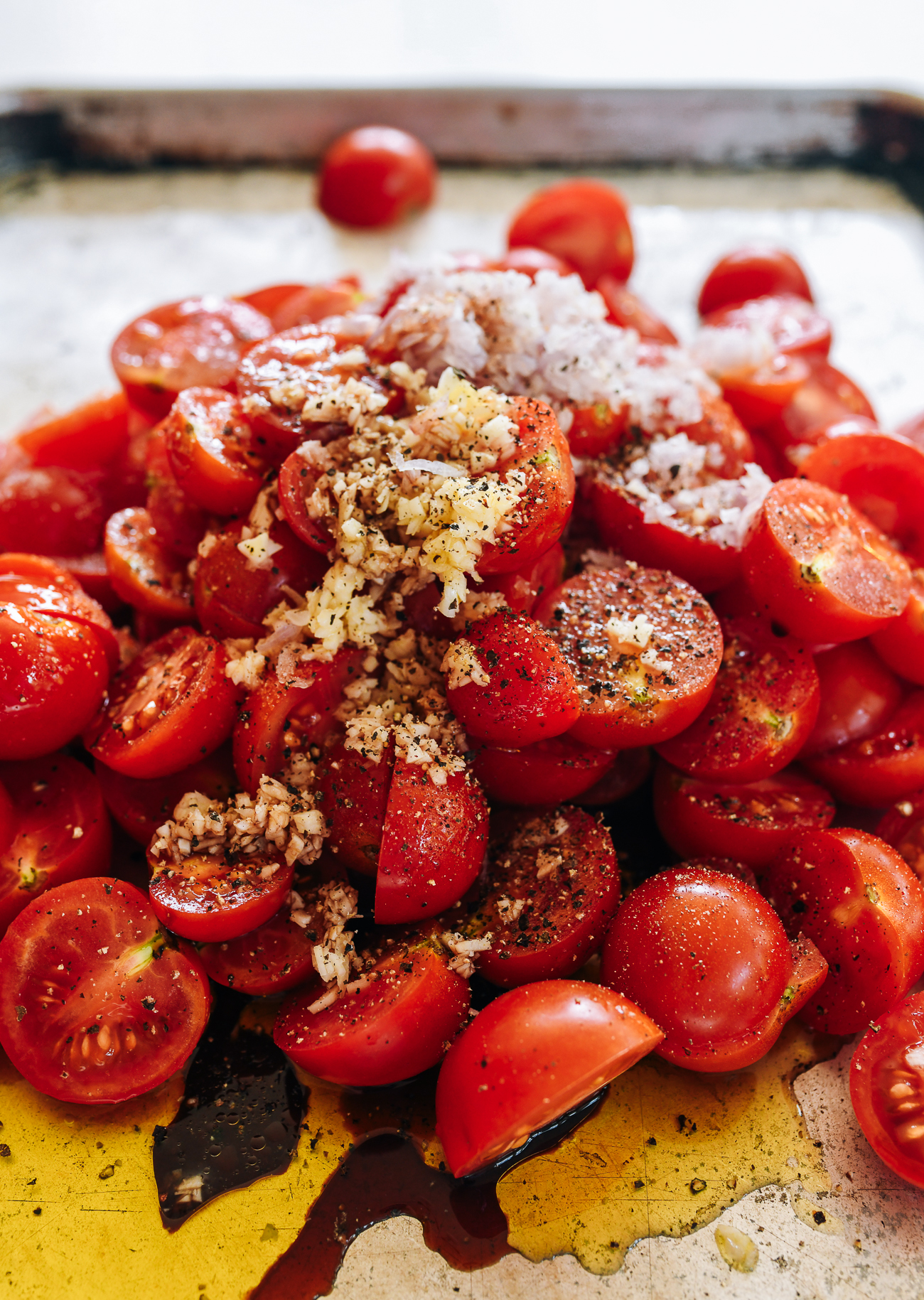 Tomatoes on sheet pan with seasonings, ready for oven roasting