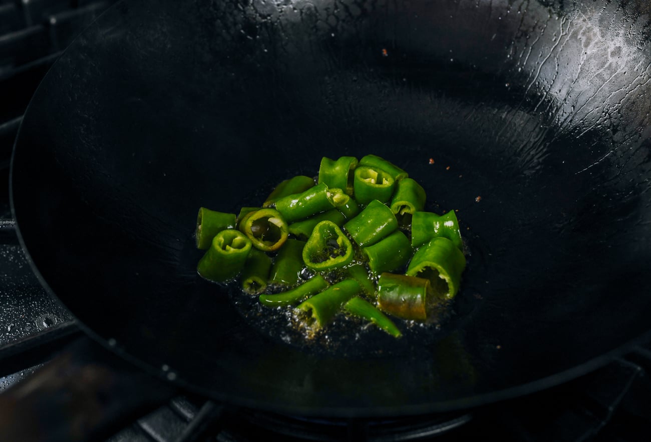 cooking long hot green peppers in a wok with oil