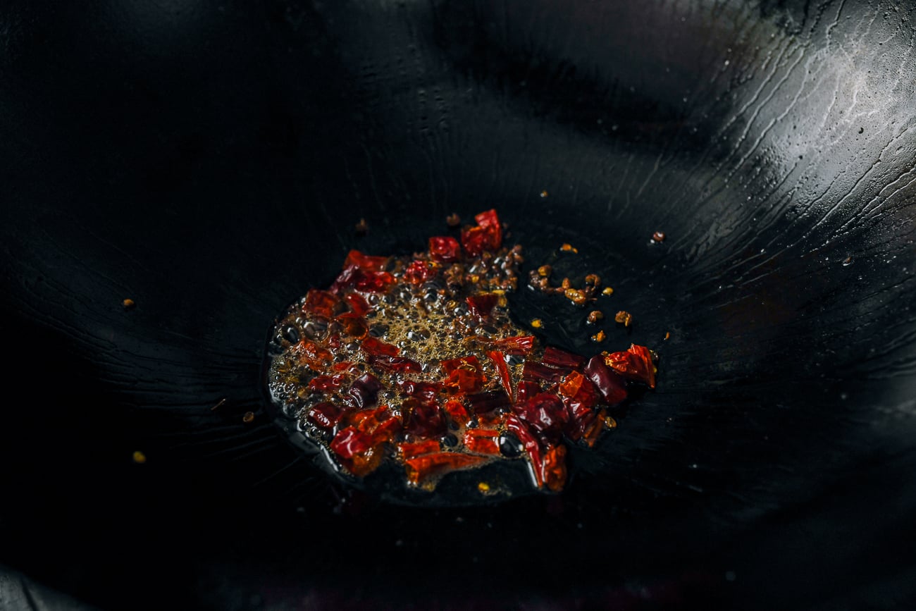 toasting dried red chili and sichuan peppercorns in wok with oil