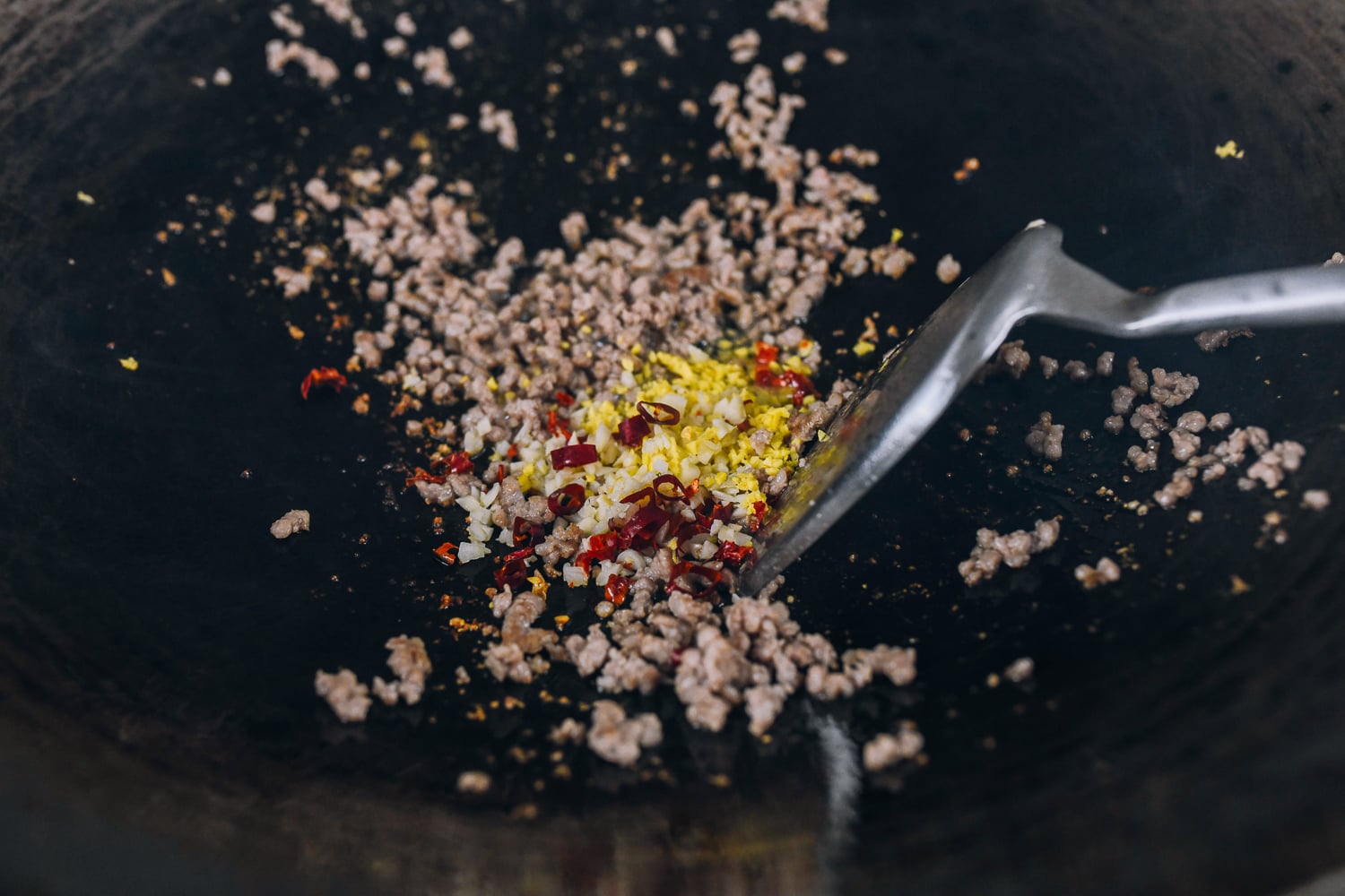 ginger and chilies added to ground pork in wok