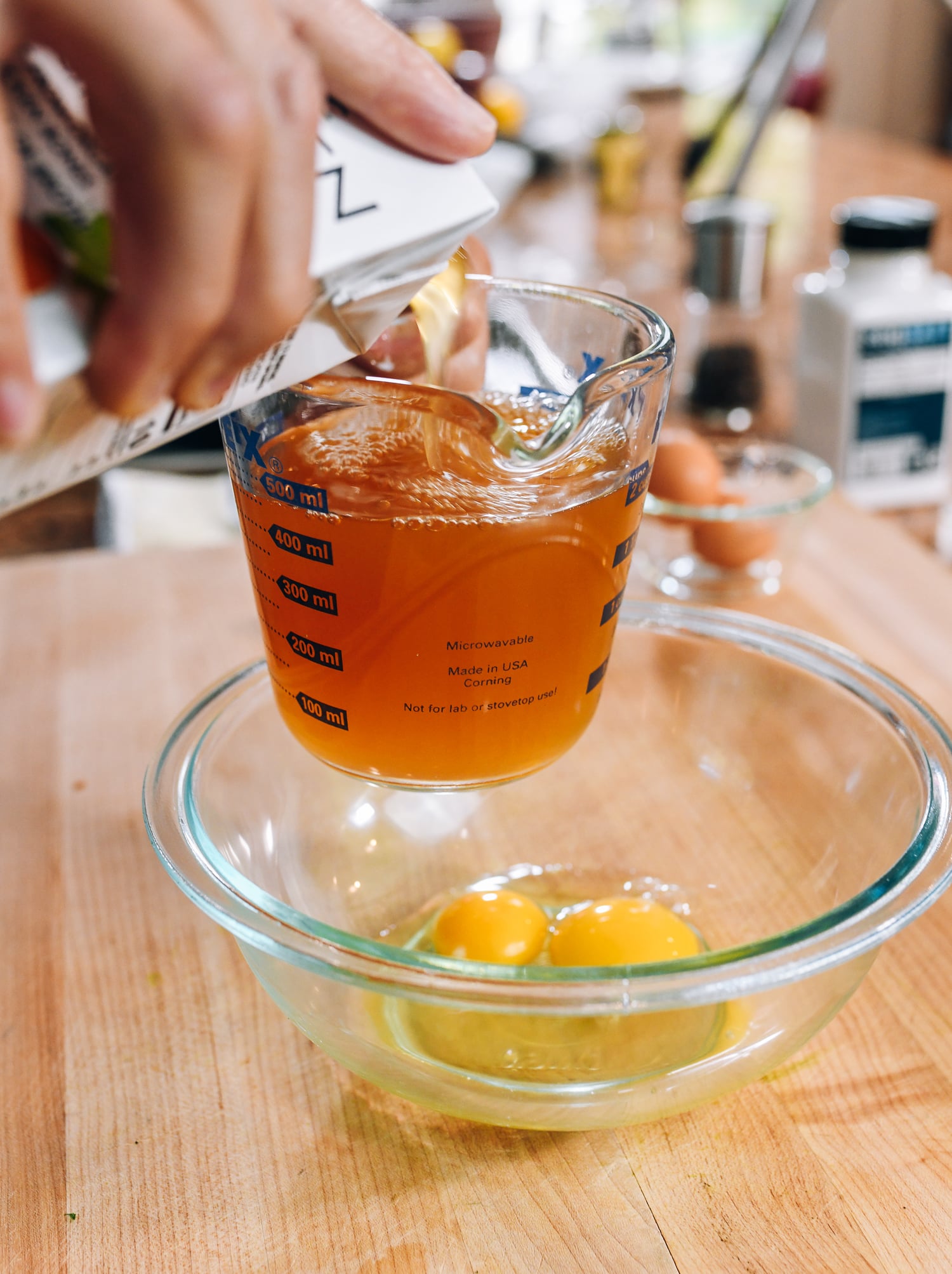 pouring chicken stock into measuring cup over bowl of eggs