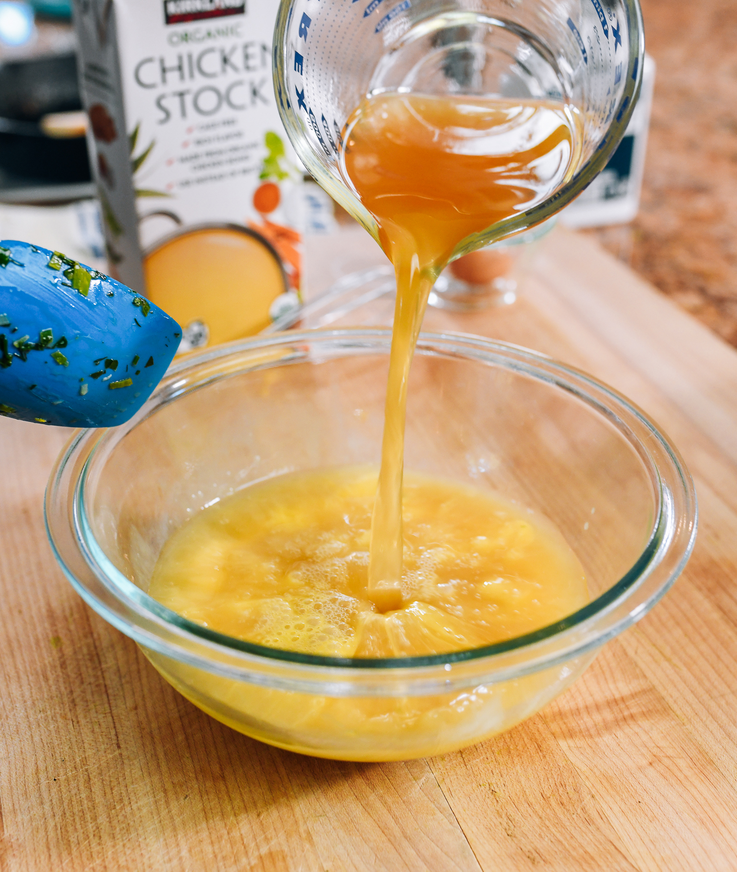 adding chicken stock to bowl of beaten eggs