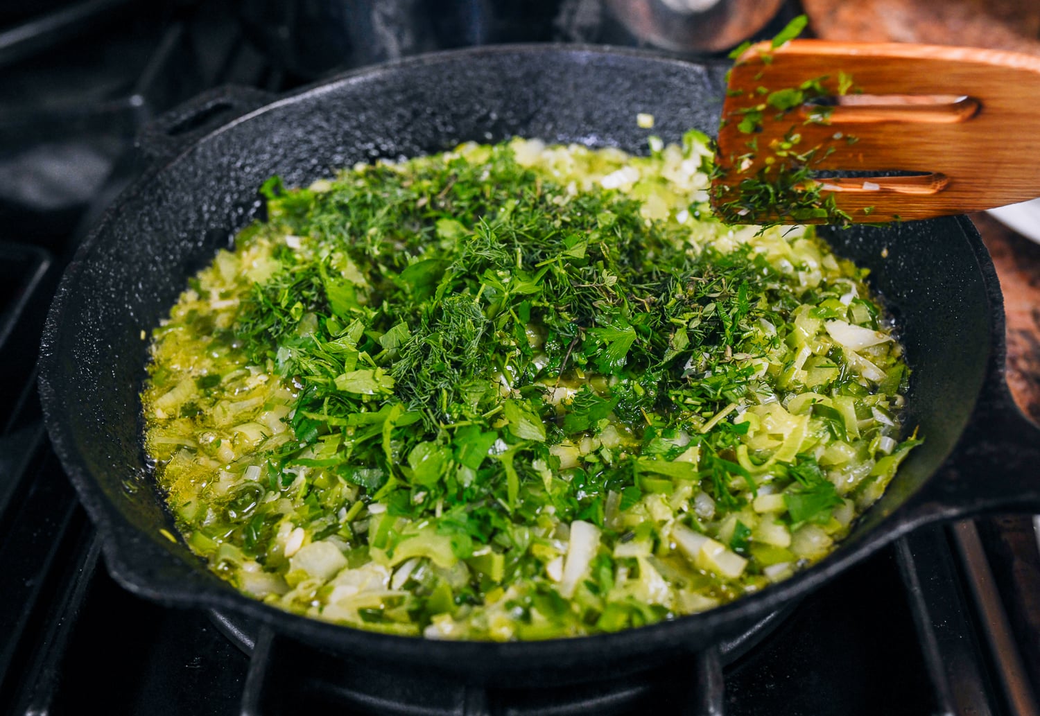 adding herbs to cooked vegetables in pan