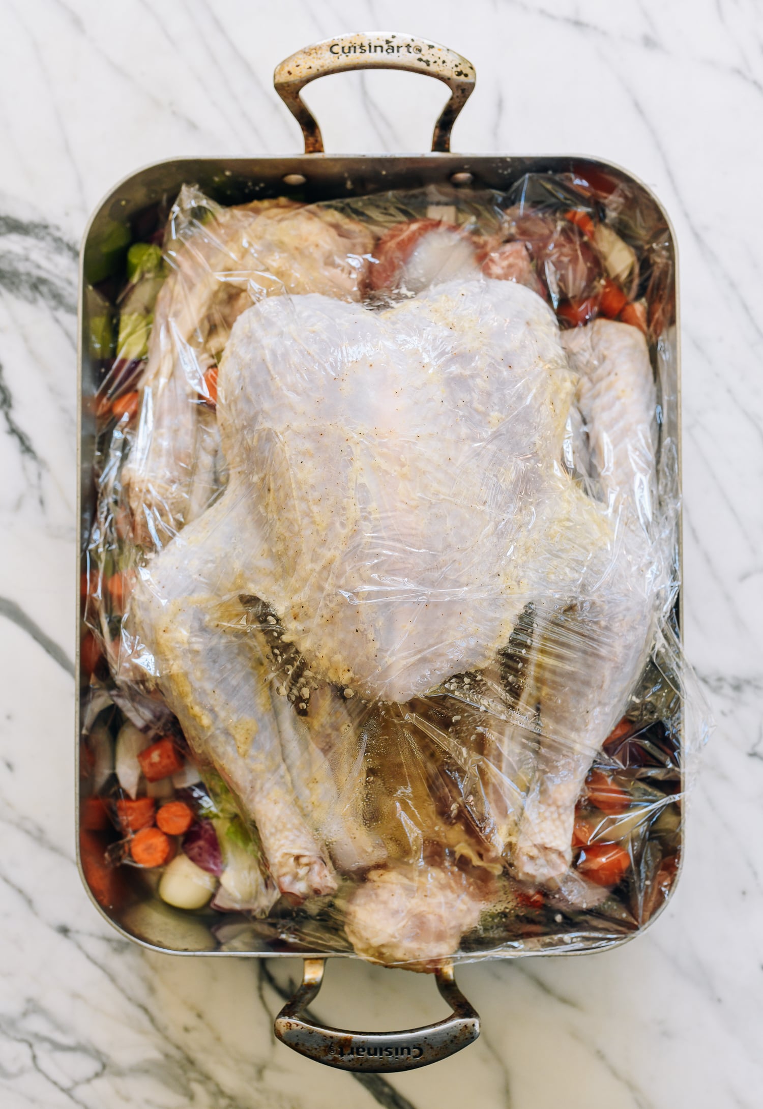 marinated turkey in roasting pan with plastic wrap