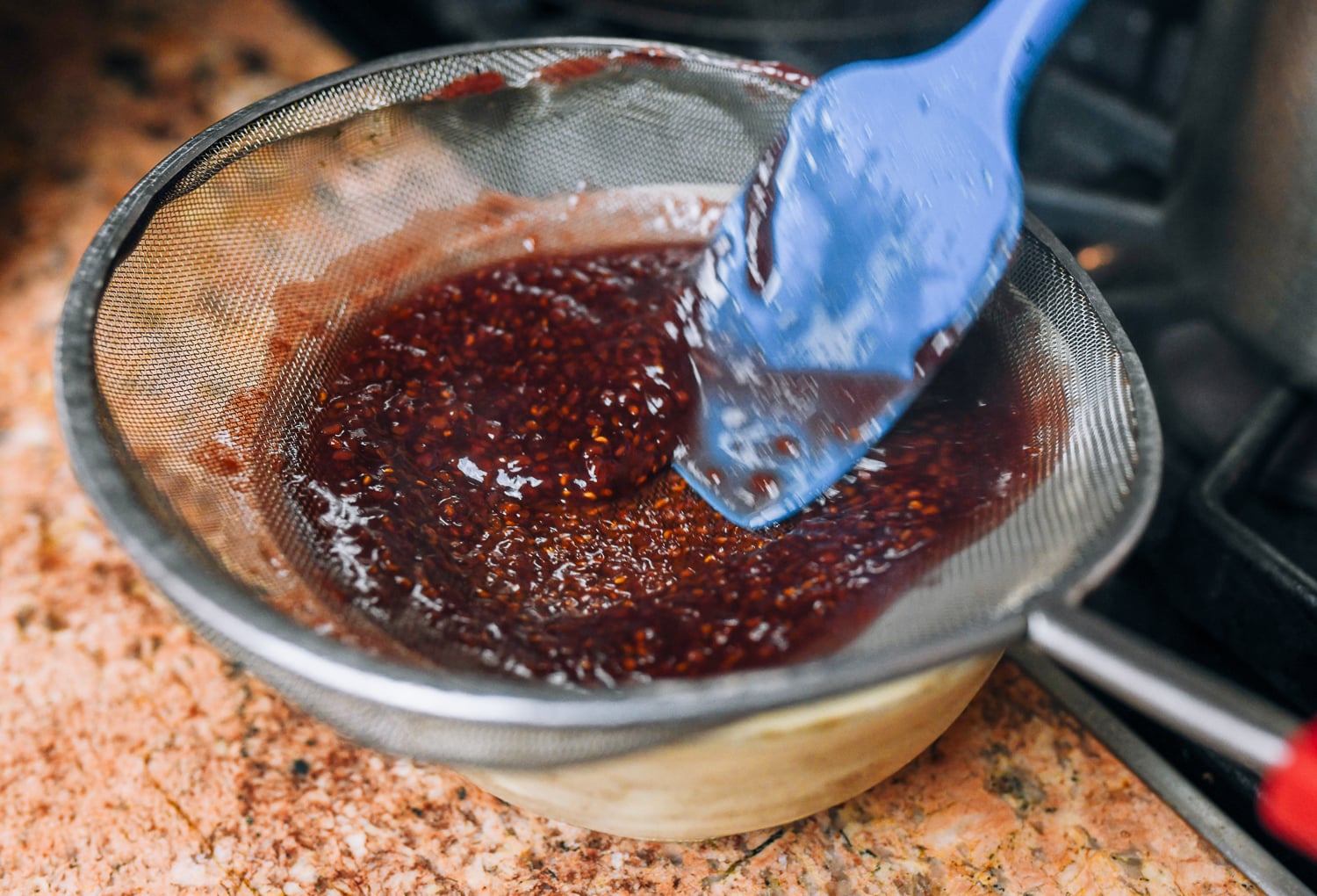 pushing raspberry jam through a sieve to remove seeds