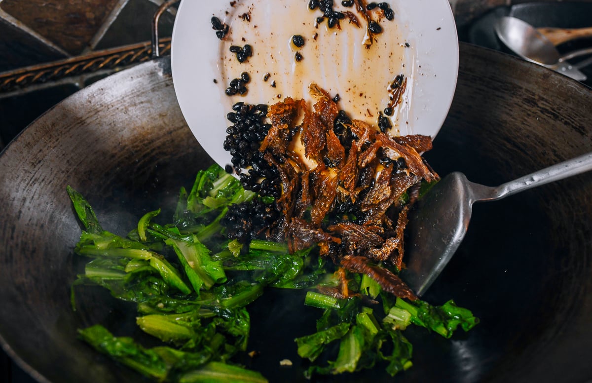 adding dace to leafy greens in wok