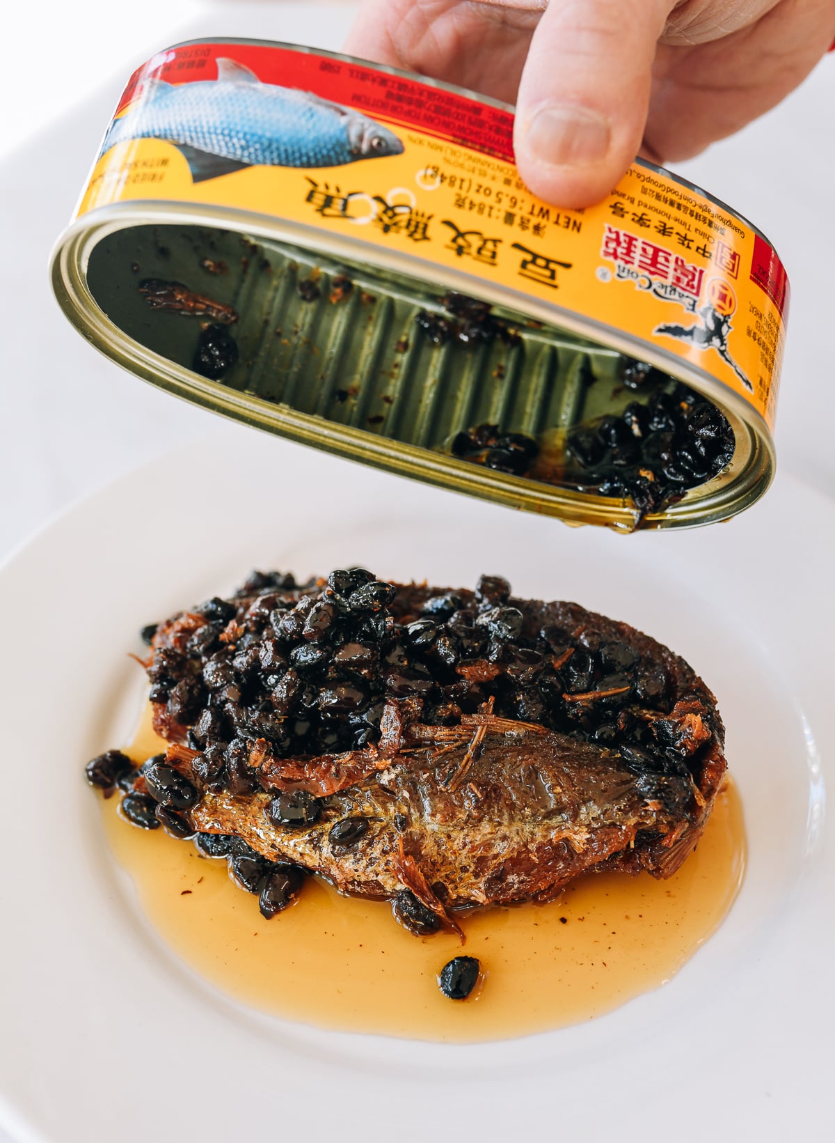 pouring fried dace with fermented black bean out of can and onto white plate