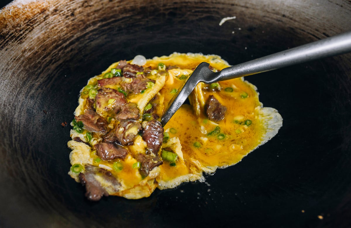 pushing beaten eggs around wok with a wok spatula