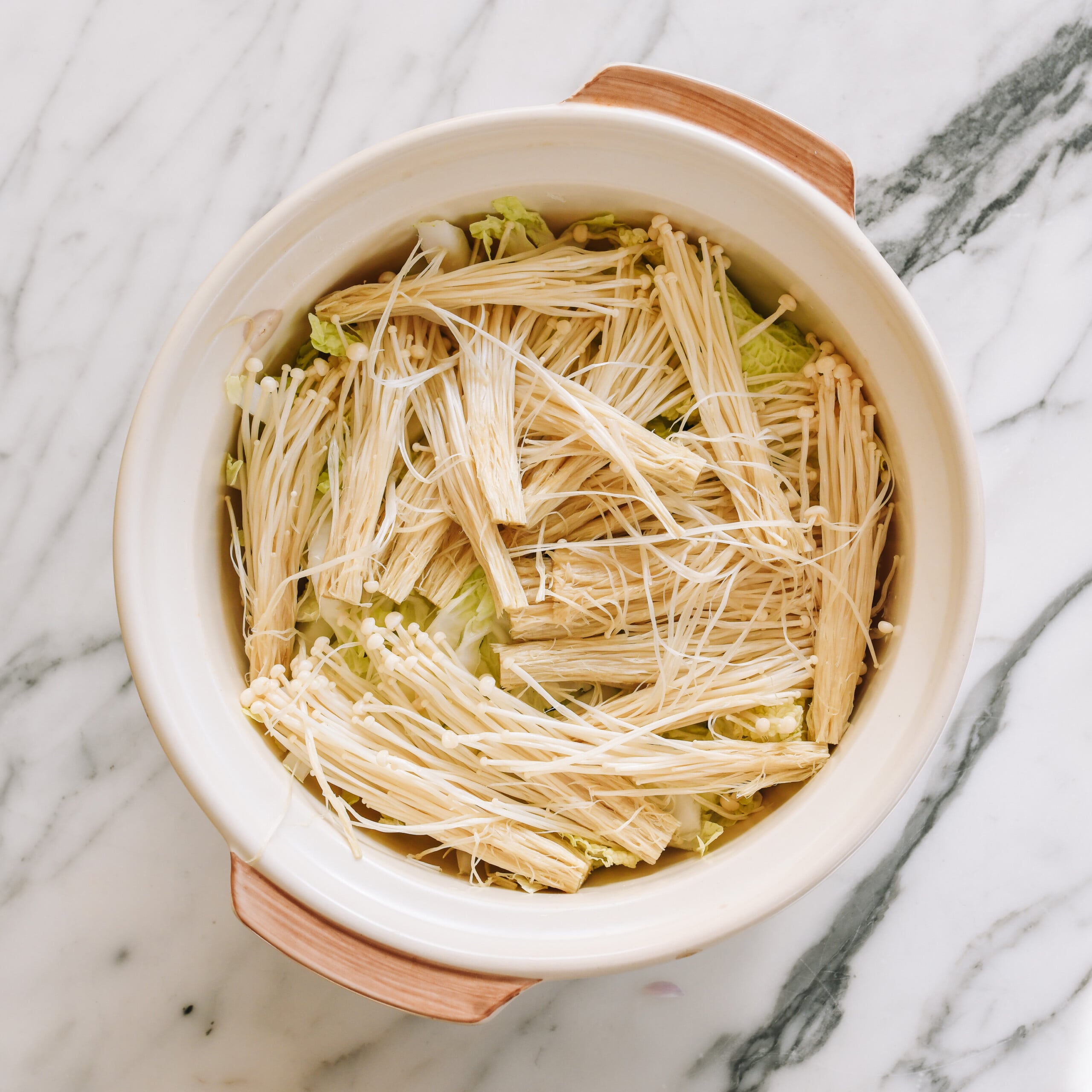 enoki mushrooms layered on top of vegetables in clay pot