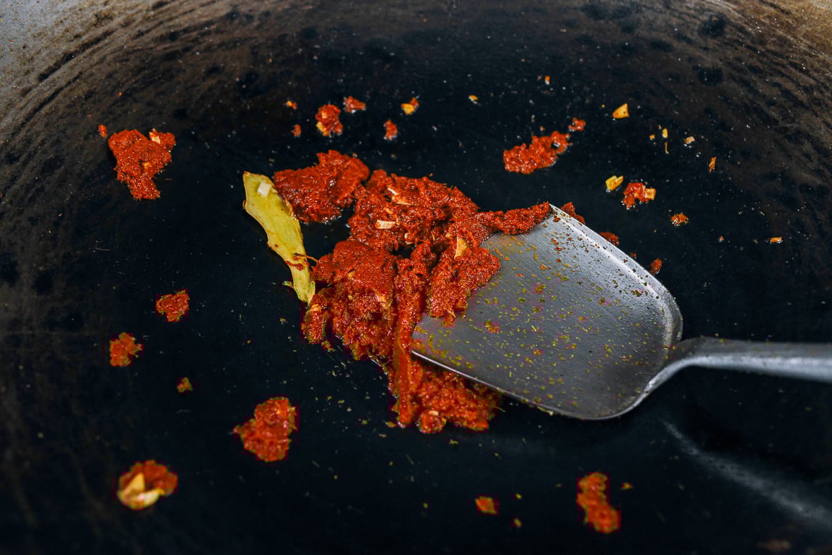 cooking thai red curry paste in wok with ginger and garlic