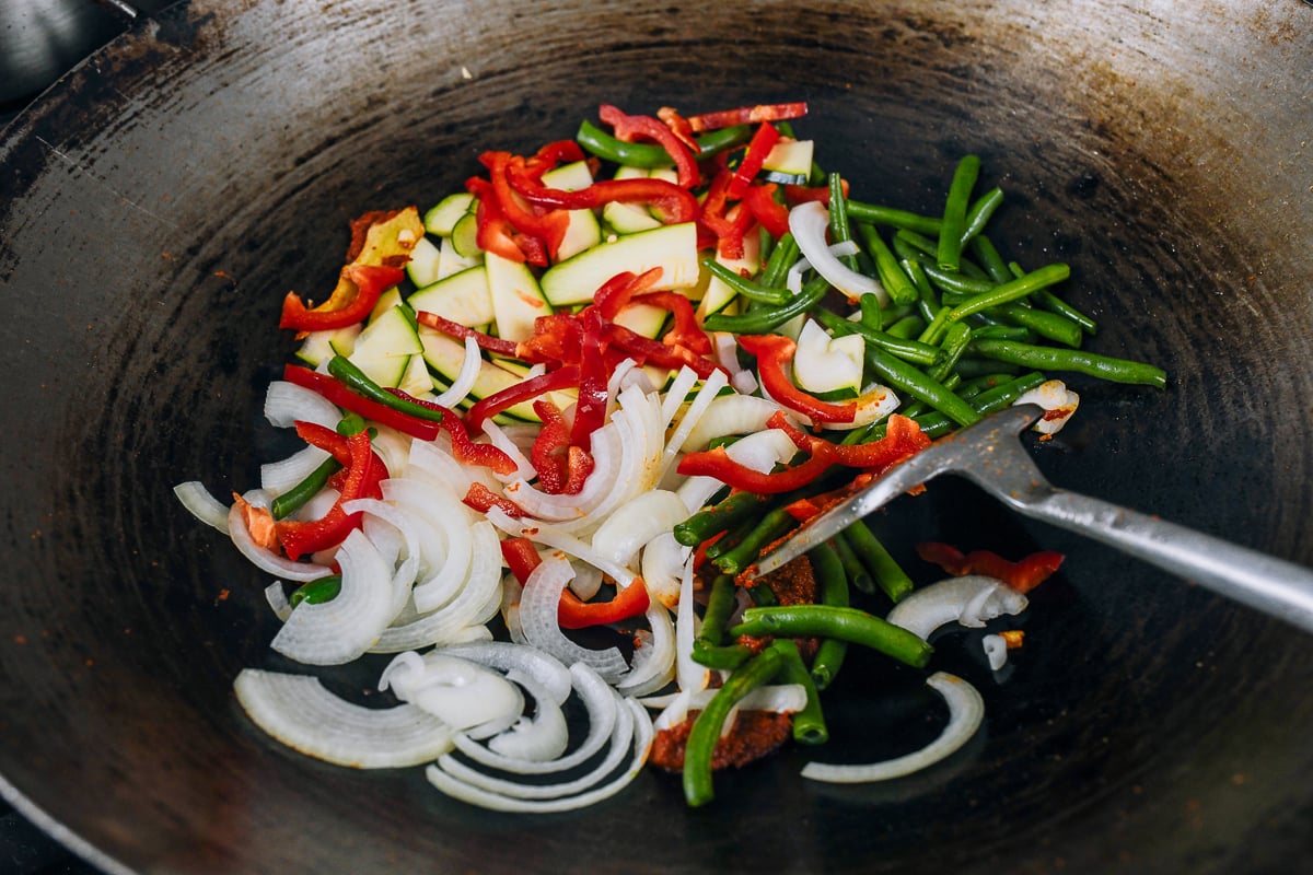 adding vegetables to wok with curry paste