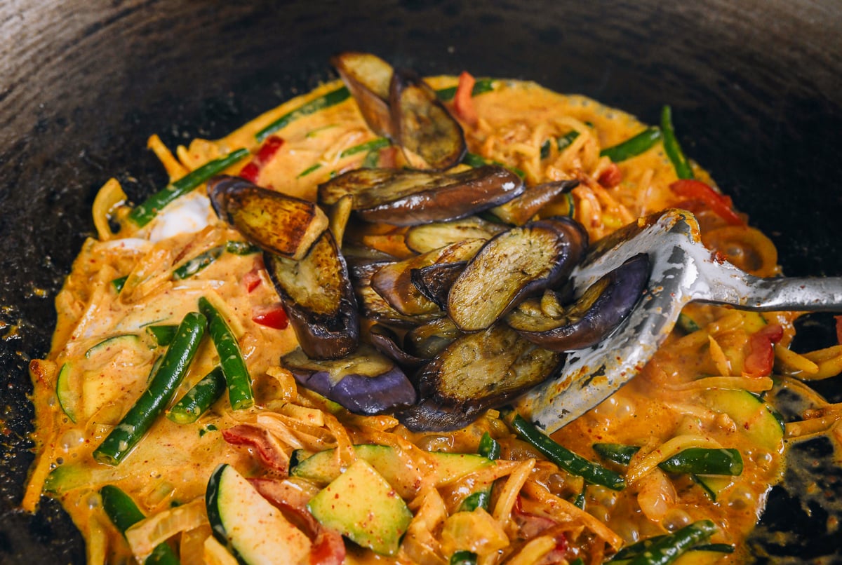 adding eggplant to vegetables simmering in coconut red curry sauce
