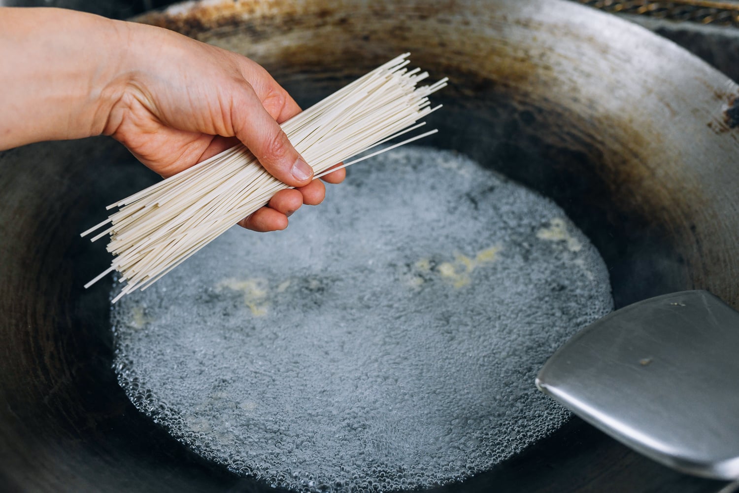 adding noodles to boiling water in wok