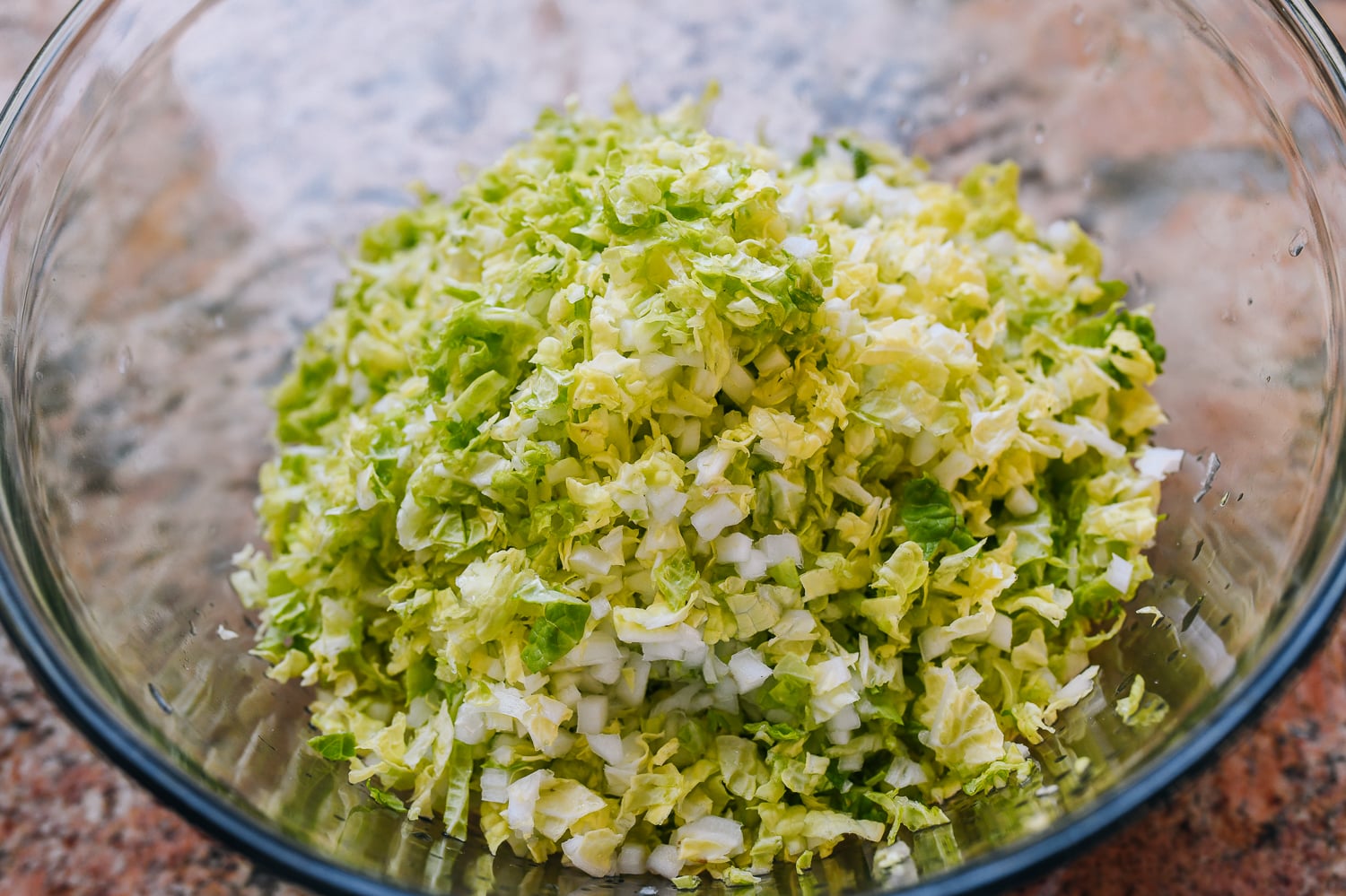 salting chopped cabbage in glass bowl