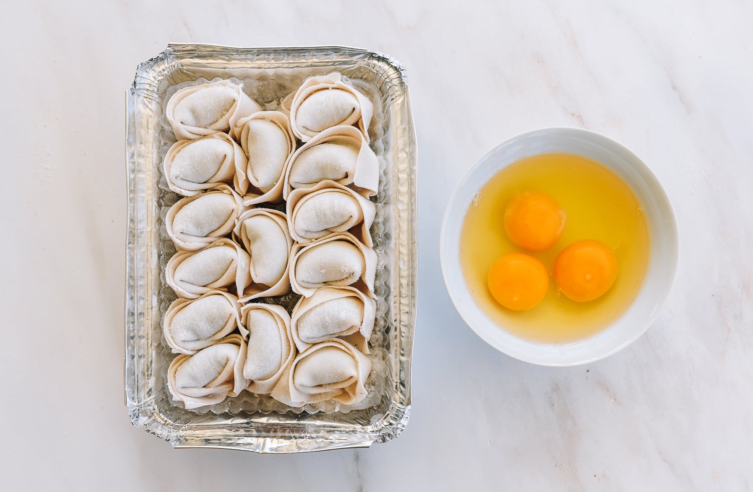 frozen wontons in foil tray and bowl of cracked eggs