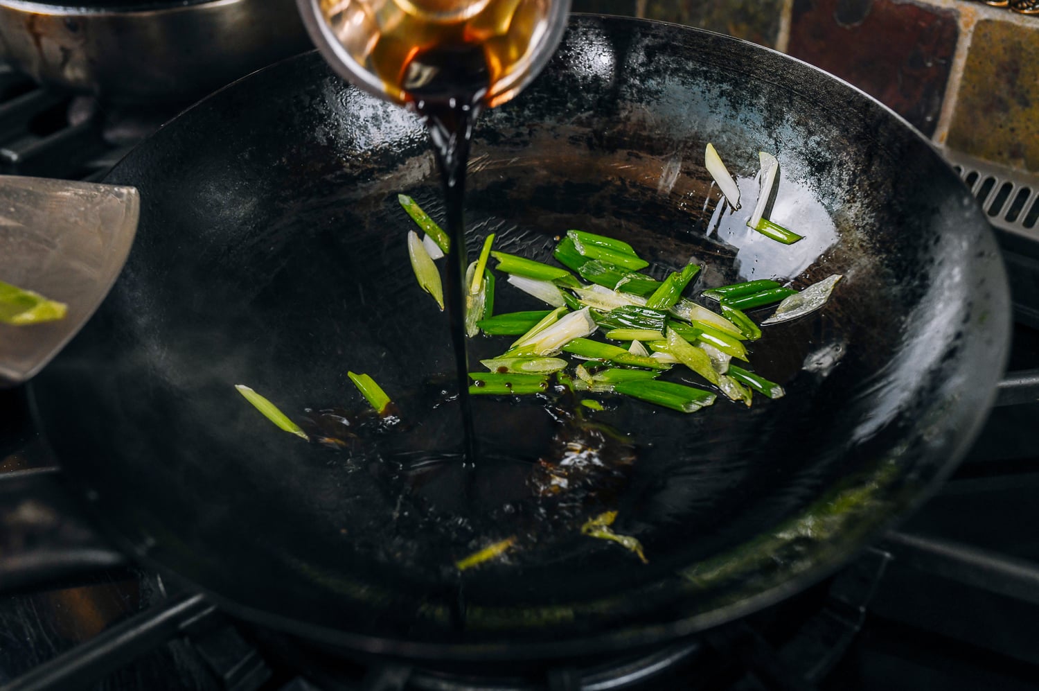 adding soy sauce to scallions and oil in wok