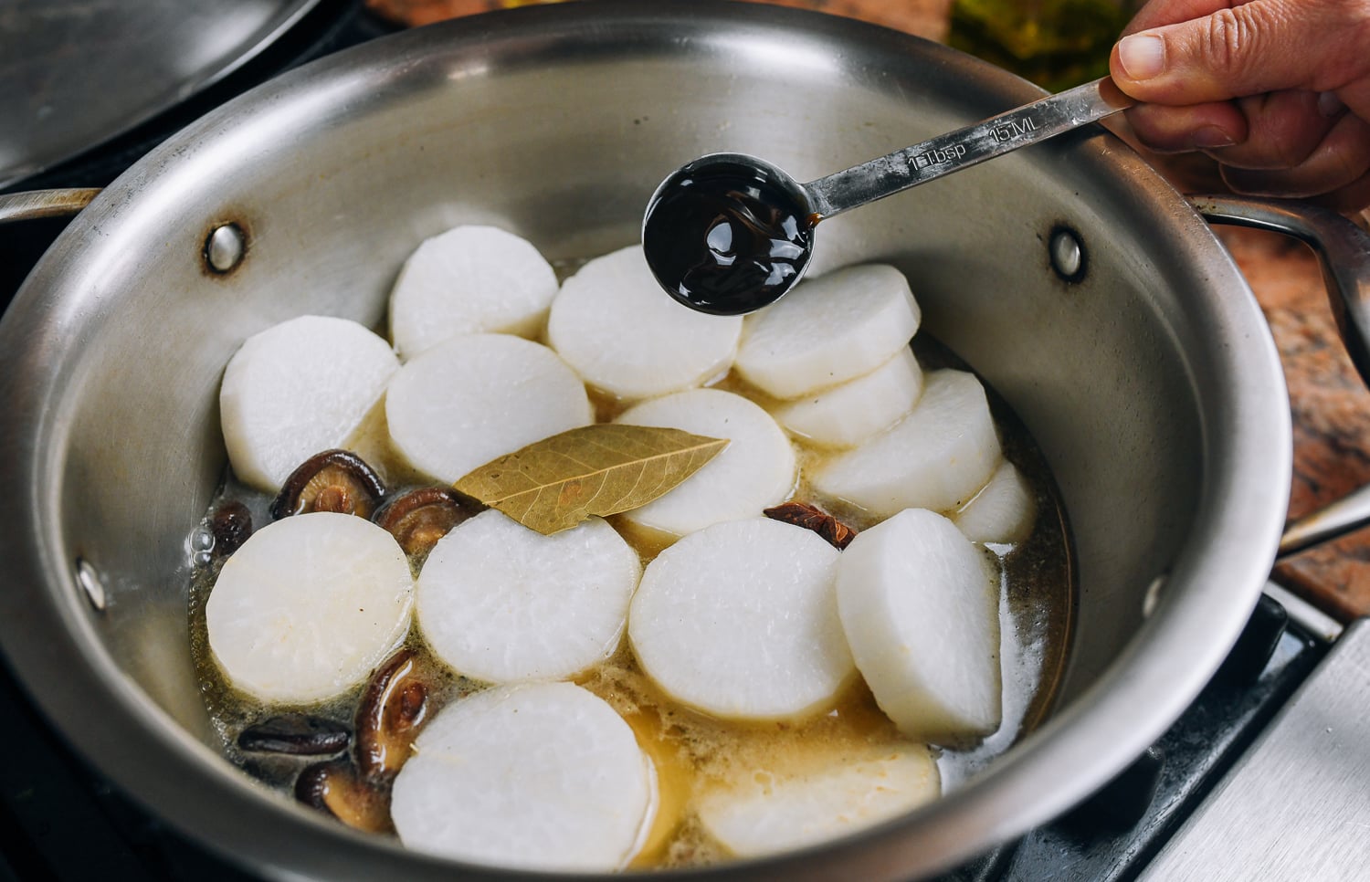 adding oyster sauce to daikon radish and mushrooms in pot