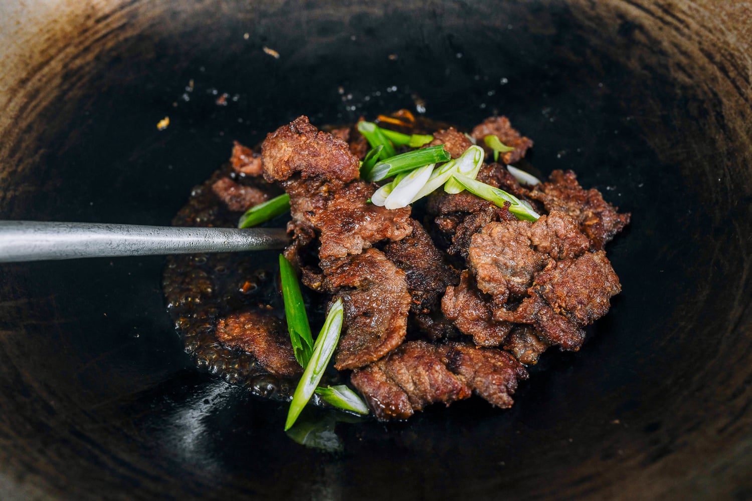 adding sliced beef to wok with sauce