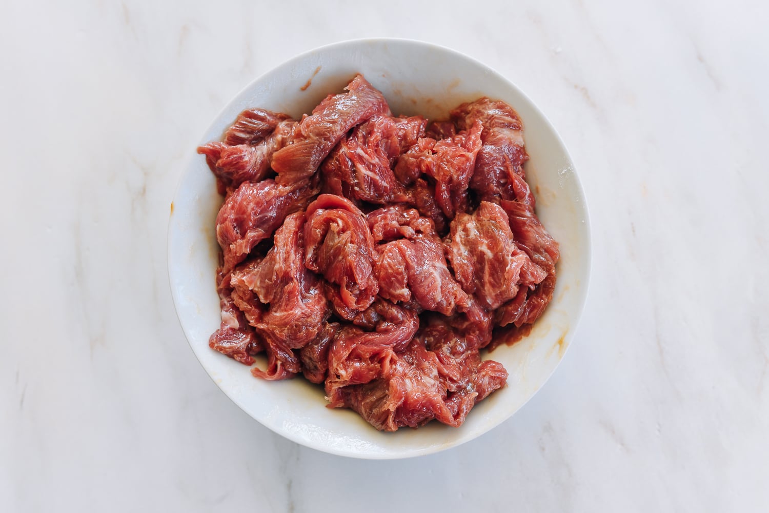 marinated sliced flank steak in white bowl