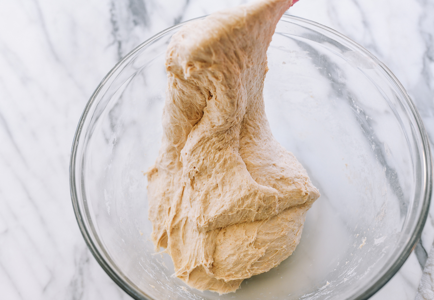 Lifting, stretching, and folding dough with rubber spatula in glass bowl