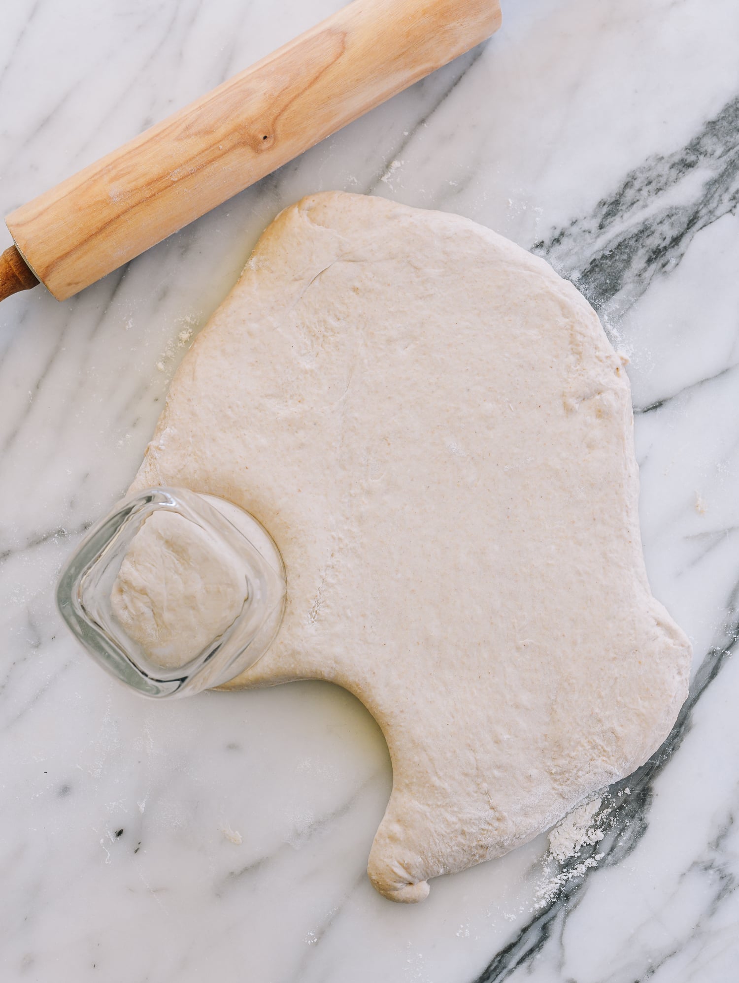 dough rolled out on marble countertop, cutting circles with a water glass