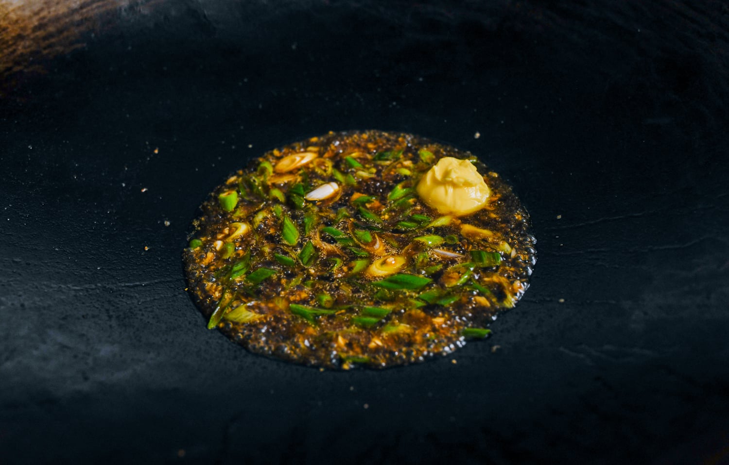adding butter to soy sauce, scallions, garlic, in wok