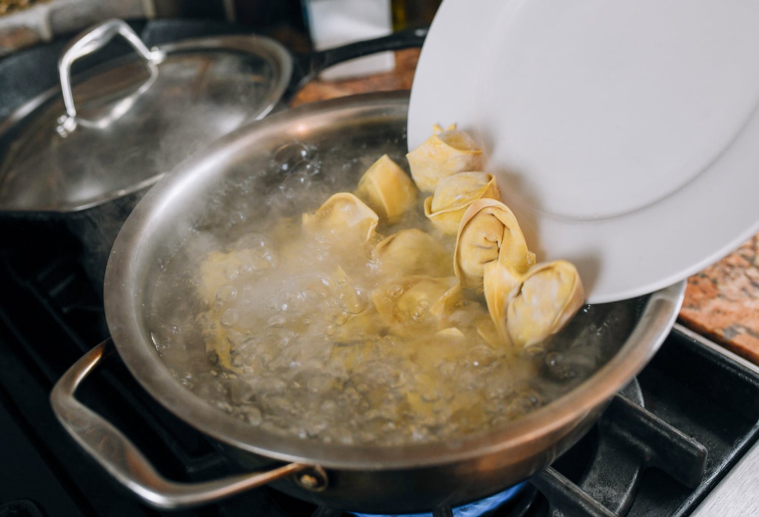 pouring frozen wontons from plate into pot of boiling water