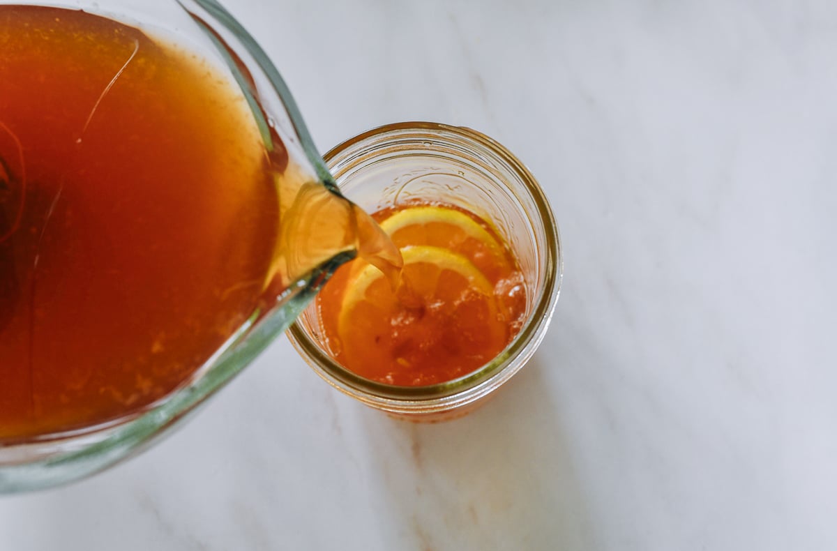 pouring iced tea into glass over ice, with lemon slices