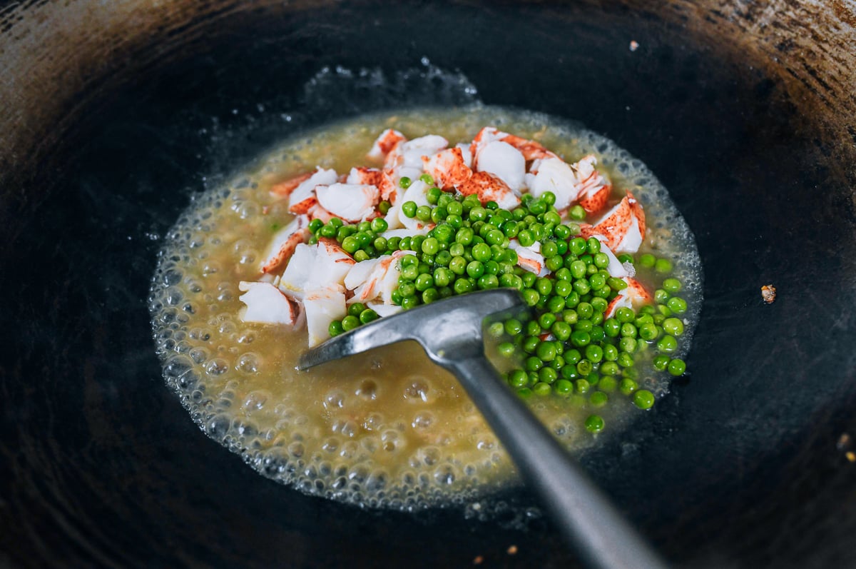 adding lobster and peas to sauce in wok
