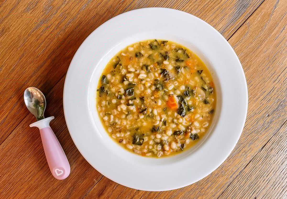 bowl of mushroom barley soup with kale and toddler spoon