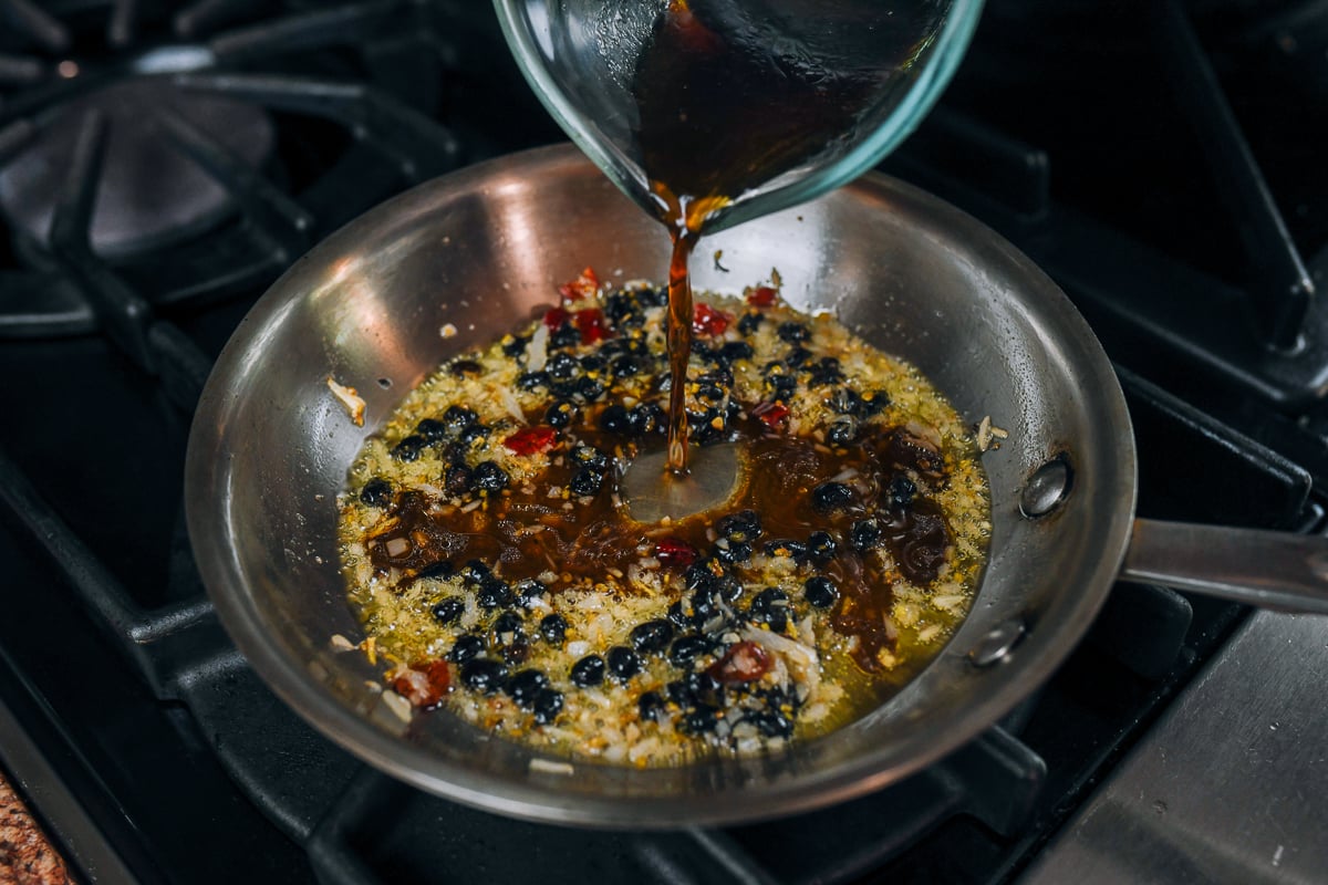 pouring sauce ingredients into pan with aromatics
