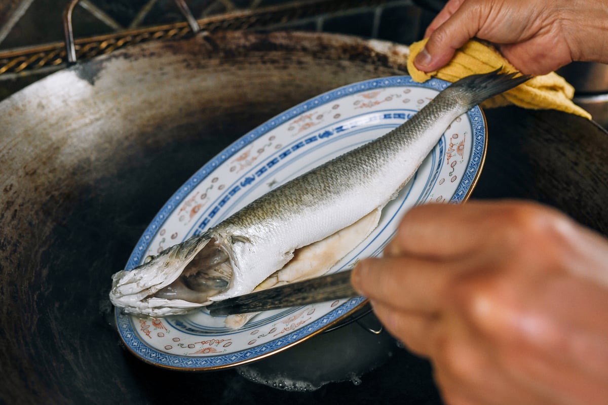 pouring off liquid from plate of steamed whole fish