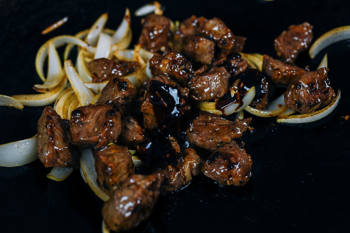 adding seasoning sauces to shaking beef in wok