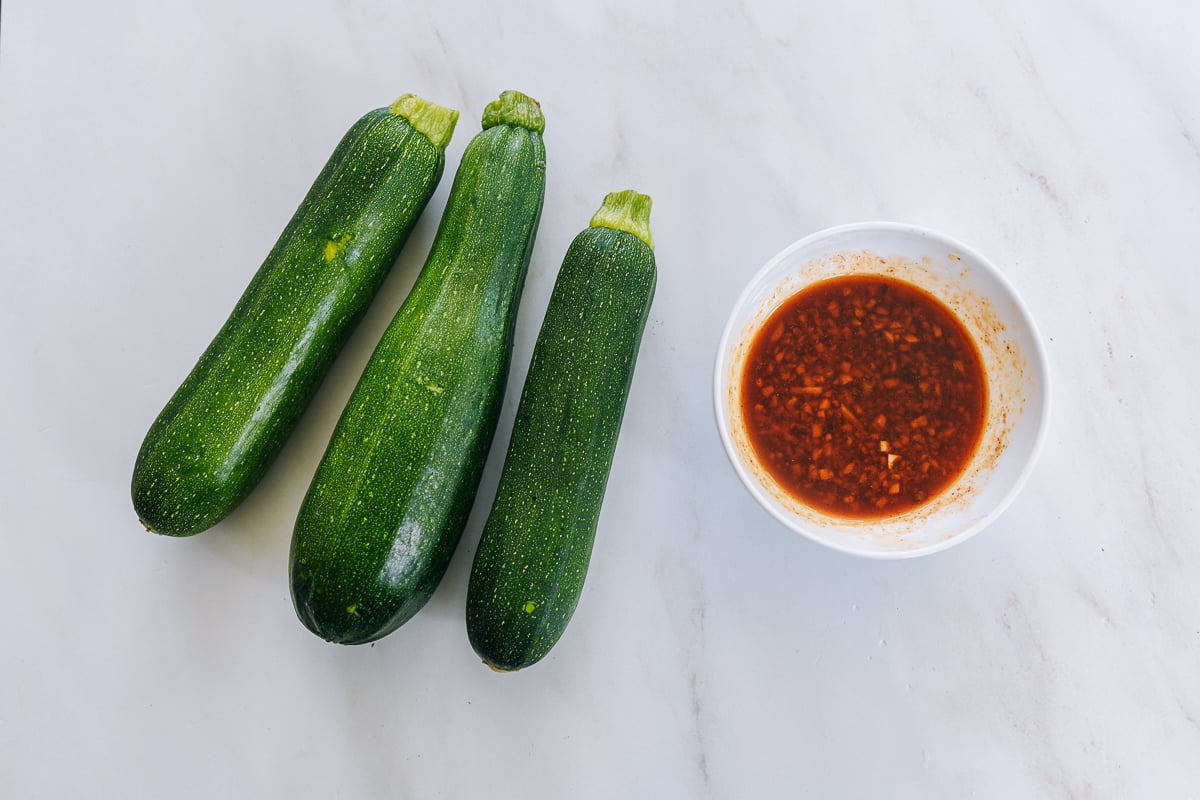 three medium zucchinis next to small bowl with chinese salad dressing