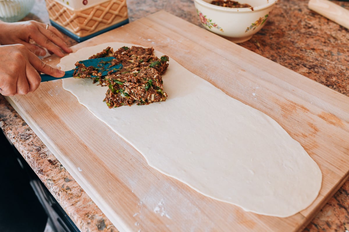 spreading meat filling on dough sheet