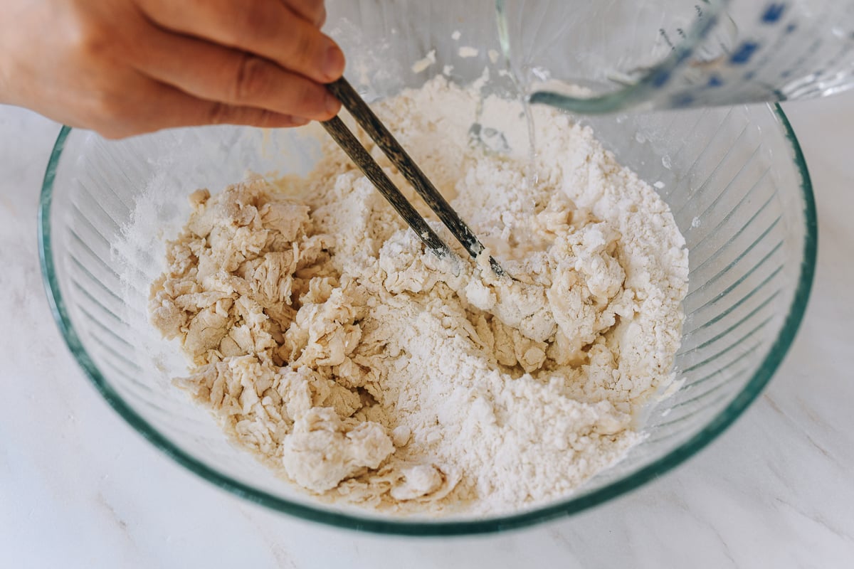 mixing dough with chopsticks while adding water to flour